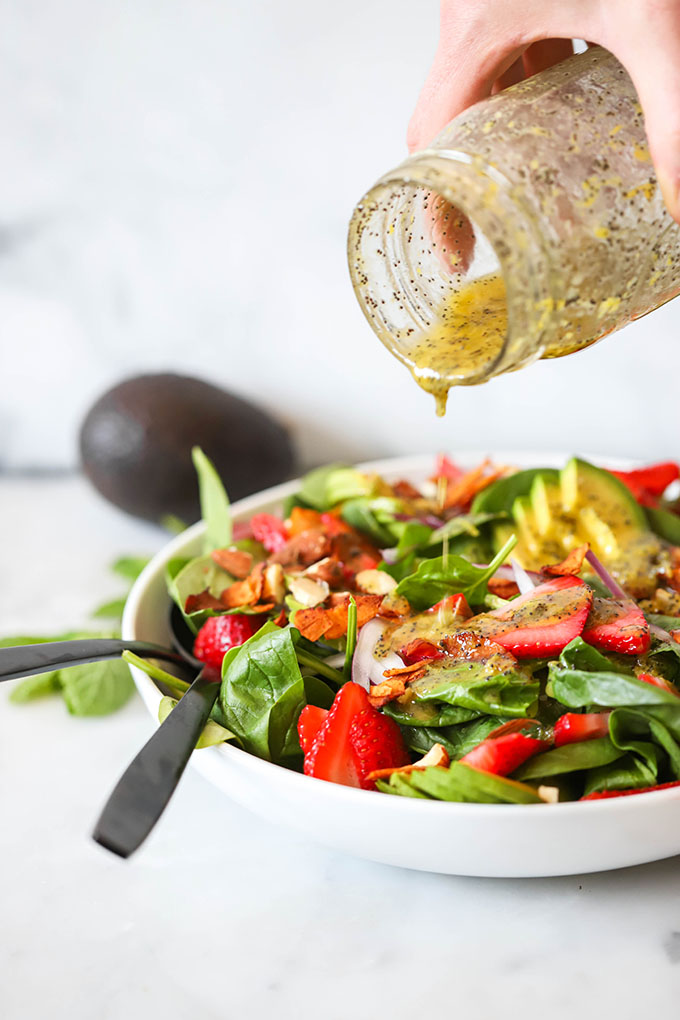 Vegan strawberry spinach salad with lemon poppyseed dressing being poured over top from a mason jar.