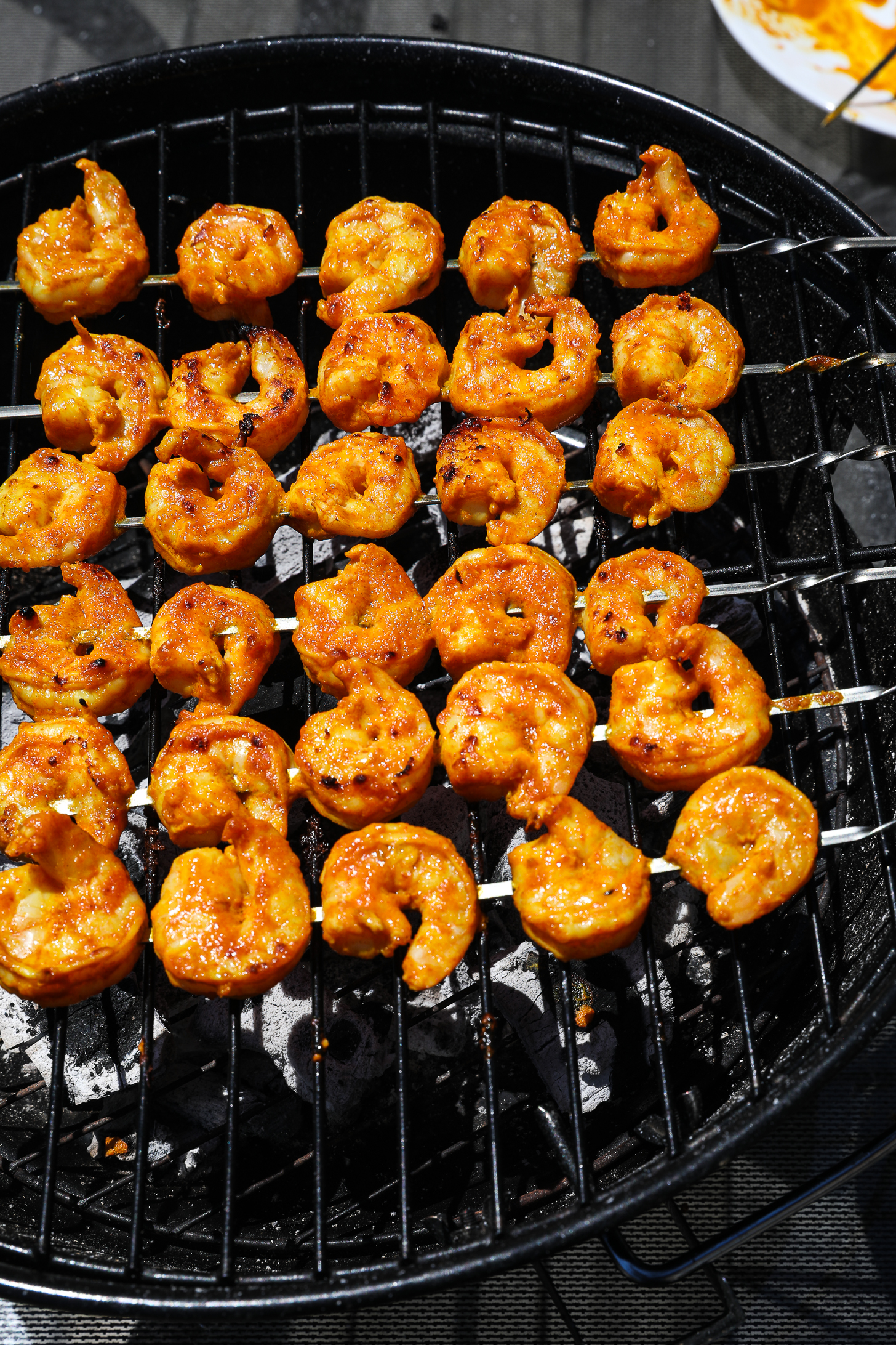 Six spicy charred shrimp skewers on a charcoal grill.