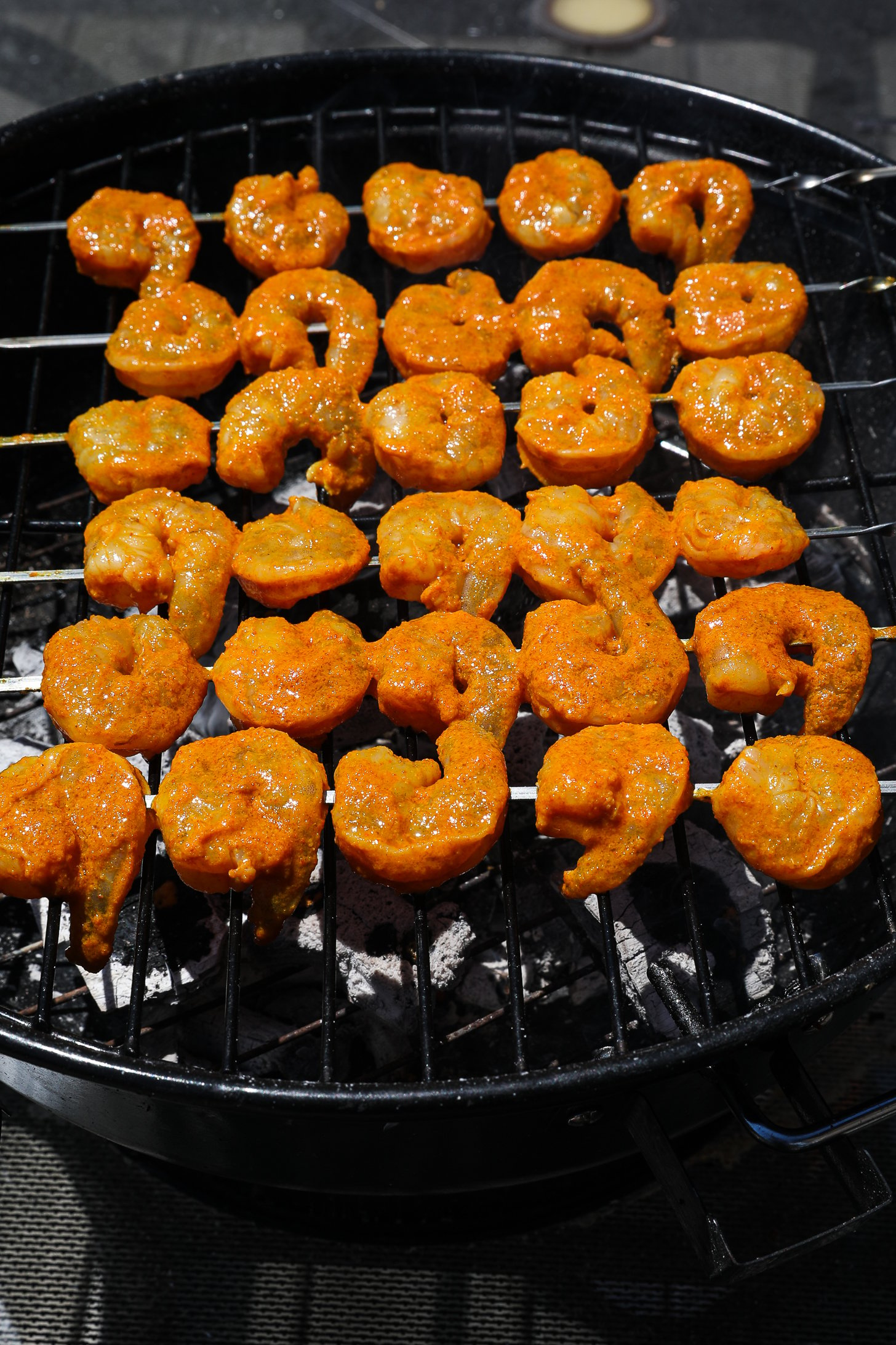 Six spice-coated shrimp skewers on a charcoal grill.