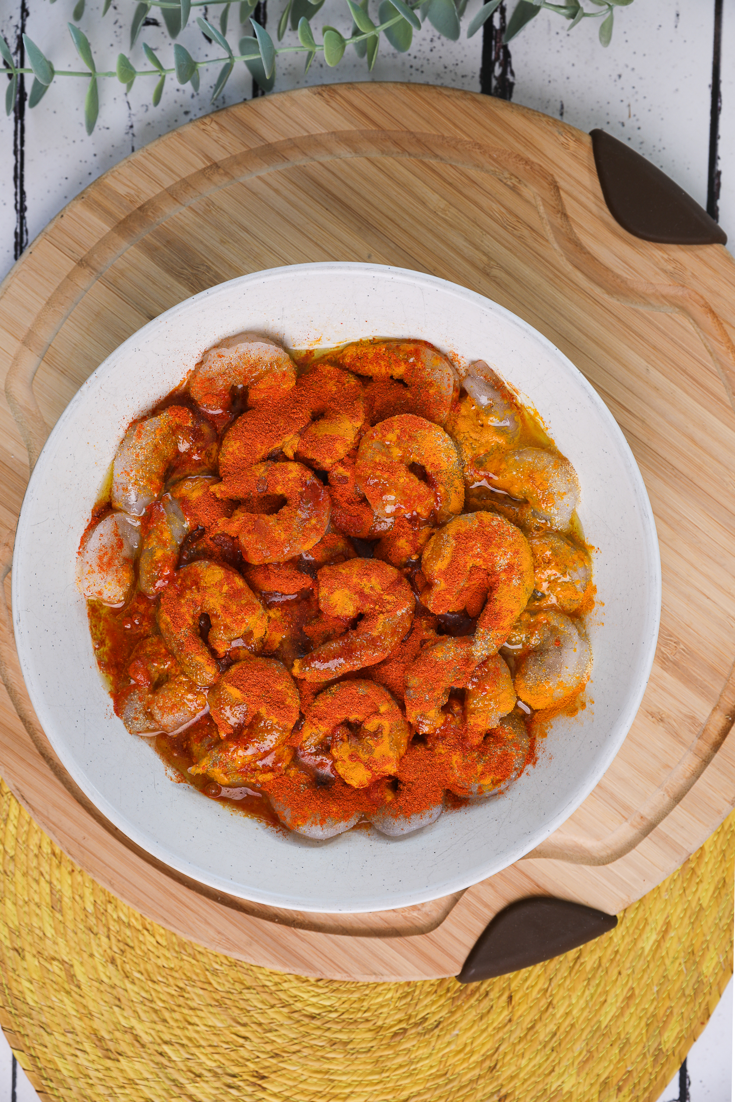 A bowlful of raw shrimp topped with lots of spices and turmeric, oil and lime juice.