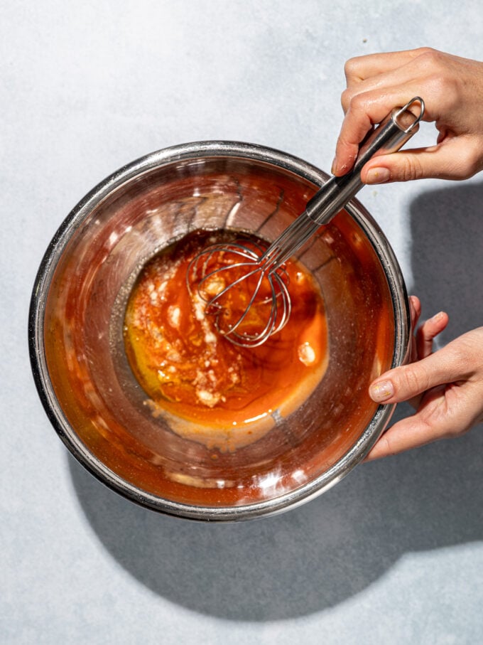 hand whisking buffalo sauce in metal bowl