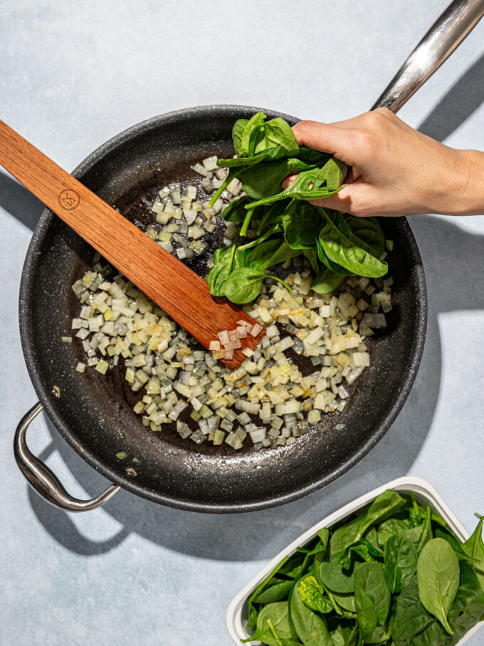 hand adding spinach to skillet