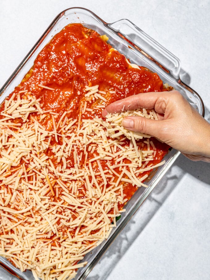 hand adding cheese to lasagna