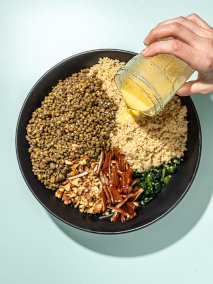 hand pouring lemon dressing over quinoa salad