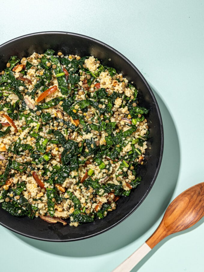 kale, lentil and quinoa salad in black bowl with wooden spoon