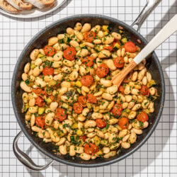 white bean and tomatoes in skillet with plate of sliced bread