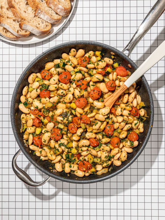 white bean and tomatoes in skillet with plate of sliced bread